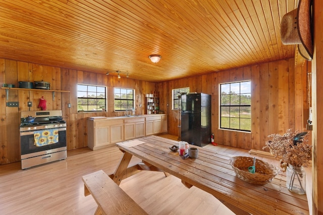 dining space with light hardwood / wood-style floors, wooden ceiling, wood walls, and a healthy amount of sunlight