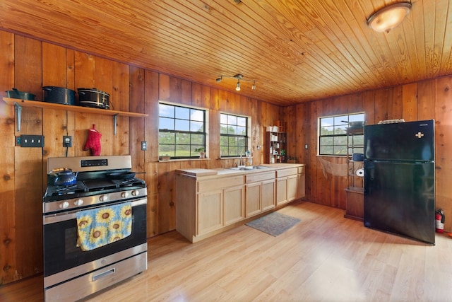 kitchen with wooden walls, light wood-type flooring, stainless steel range with gas cooktop, wood ceiling, and black fridge