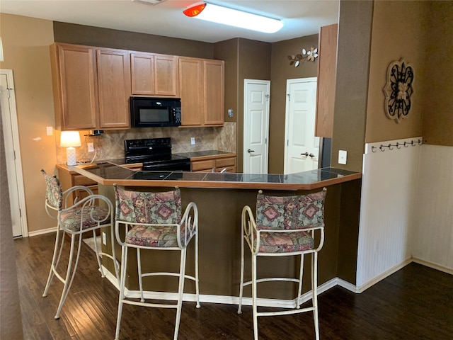 kitchen featuring black appliances, tasteful backsplash, a kitchen bar, dark hardwood / wood-style floors, and kitchen peninsula