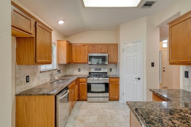 kitchen featuring lofted ceiling, stainless steel appliances, dark stone counters, and sink