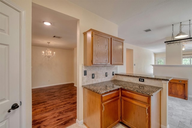 kitchen with hanging light fixtures, an inviting chandelier, backsplash, kitchen peninsula, and dark stone counters