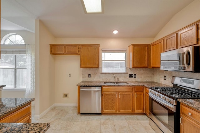 kitchen with dark stone countertops, sink, lofted ceiling, and stainless steel appliances