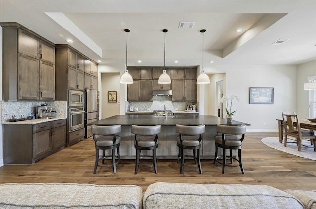 kitchen featuring appliances with stainless steel finishes, a tray ceiling, decorative light fixtures, and dark wood-type flooring