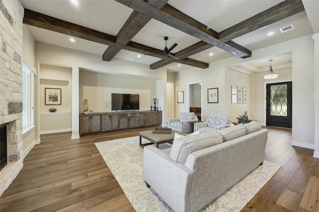 living room with beam ceiling, dark hardwood / wood-style flooring, a stone fireplace, and coffered ceiling