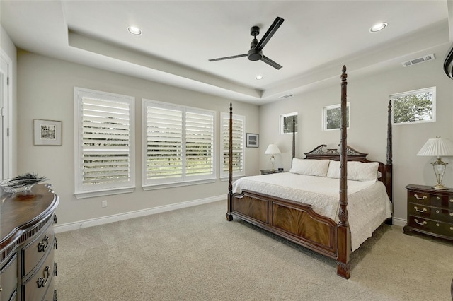 bedroom with light colored carpet, a raised ceiling, and ceiling fan