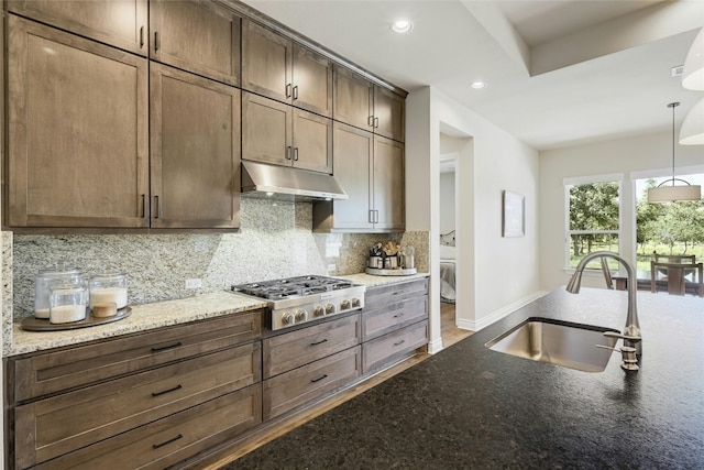 kitchen with light stone countertops, decorative light fixtures, stainless steel gas cooktop, and sink