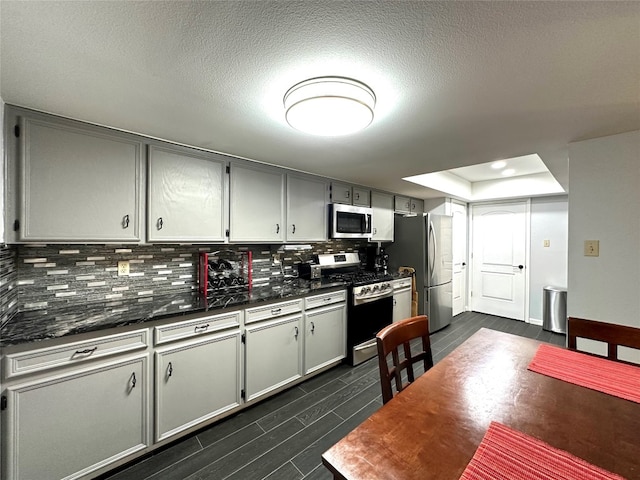 kitchen with gray cabinetry, backsplash, a raised ceiling, and appliances with stainless steel finishes