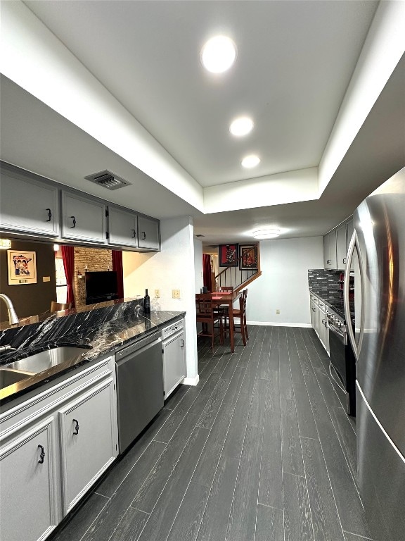 kitchen featuring a raised ceiling, sink, gray cabinetry, appliances with stainless steel finishes, and dark hardwood / wood-style floors