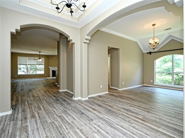 empty room with a notable chandelier, crown molding, wood-type flooring, lofted ceiling, and a tray ceiling