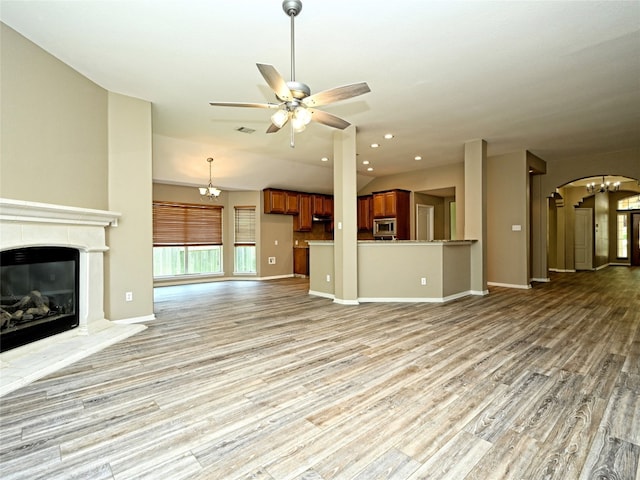 unfurnished living room featuring ceiling fan with notable chandelier, light hardwood / wood-style flooring, and lofted ceiling