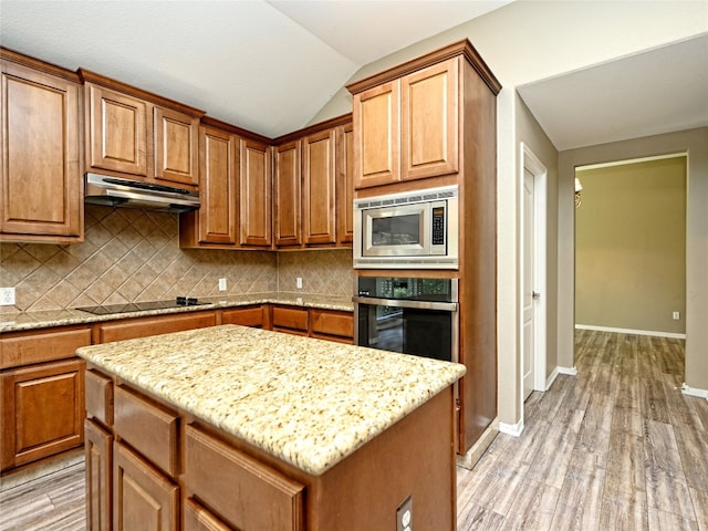 kitchen featuring light stone countertops, light hardwood / wood-style flooring, lofted ceiling, a kitchen island, and appliances with stainless steel finishes