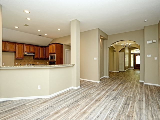 kitchen with backsplash, stainless steel microwave, light hardwood / wood-style floors, and vaulted ceiling