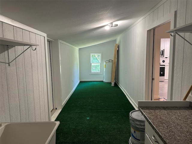 hallway featuring water heater, wood walls, dark colored carpet, lofted ceiling, and a textured ceiling