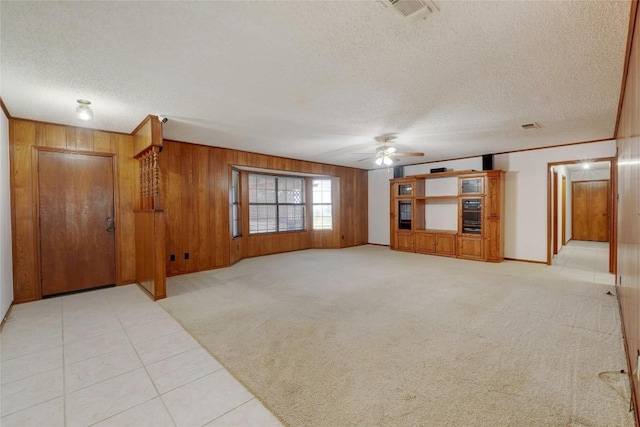 unfurnished living room with ceiling fan, light colored carpet, a textured ceiling, and wood walls