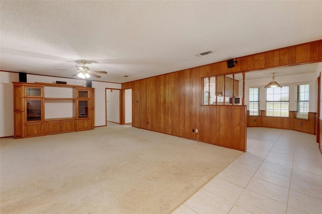 unfurnished living room with ceiling fan, a textured ceiling, light carpet, and wooden walls