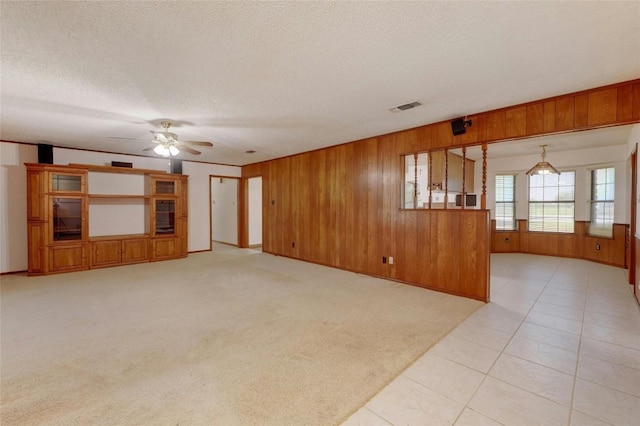 unfurnished living room featuring ceiling fan, light colored carpet, wooden walls, and a textured ceiling