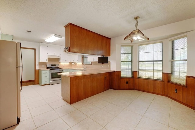 kitchen with sink, white refrigerator, hanging light fixtures, stainless steel range, and kitchen peninsula