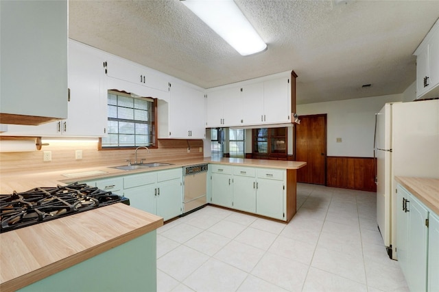 kitchen with kitchen peninsula, sink, white appliances, a textured ceiling, and wooden walls