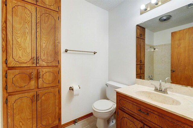 bathroom with a textured ceiling, toilet, vanity, and walk in shower