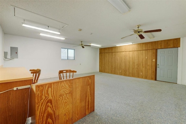 interior space featuring wooden walls, electric panel, ceiling fan, light carpet, and a textured ceiling