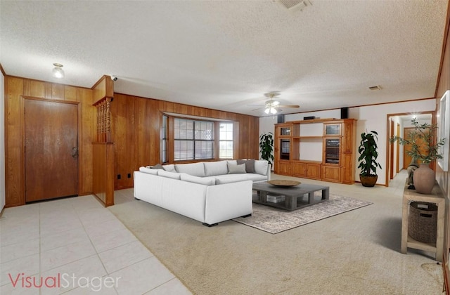 tiled living room featuring ceiling fan, wooden walls, and a textured ceiling