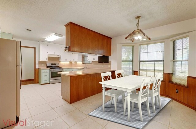 kitchen with kitchen peninsula, pendant lighting, stainless steel range, wooden walls, and white fridge