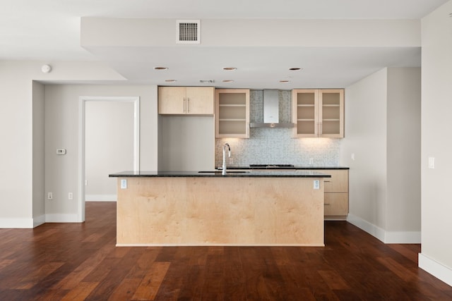 kitchen featuring light brown cabinetry, tasteful backsplash, a kitchen island with sink, dark wood-type flooring, and wall chimney range hood