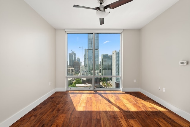 unfurnished room featuring ceiling fan, plenty of natural light, hardwood / wood-style floors, and a wall of windows