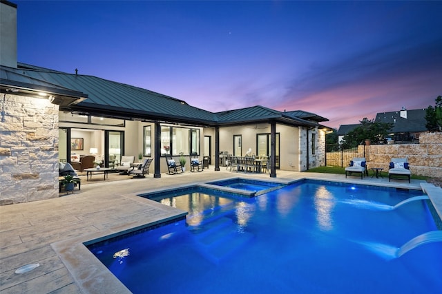 pool at dusk featuring an in ground hot tub and a patio