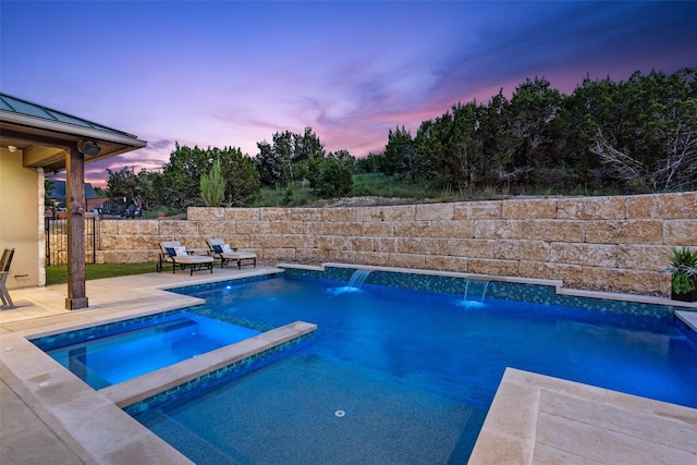 pool at dusk featuring an in ground hot tub, pool water feature, and a patio