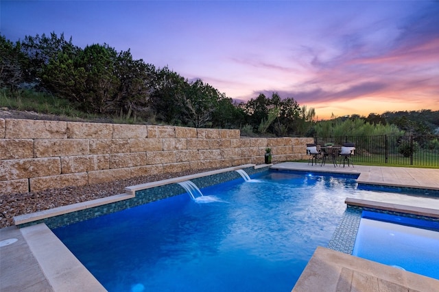 pool at dusk with a patio area and pool water feature