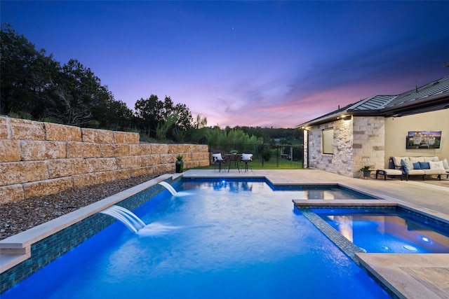 pool at dusk featuring a patio, an in ground hot tub, and pool water feature