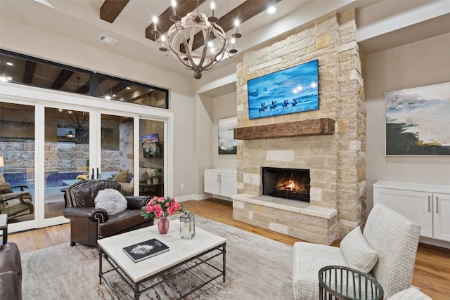 living room featuring a stone fireplace, a chandelier, light wood-type flooring, and beam ceiling