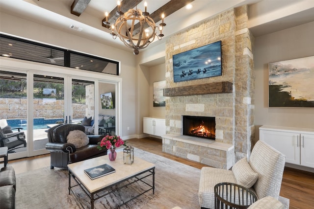 living room featuring beamed ceiling, wood-type flooring, a stone fireplace, and a chandelier