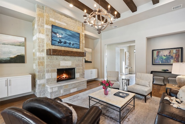 living room featuring a stone fireplace, beamed ceiling, hardwood / wood-style floors, and an inviting chandelier