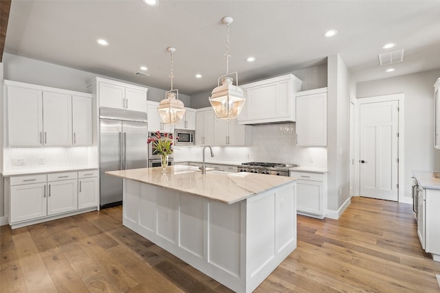 kitchen with built in appliances, light hardwood / wood-style floors, backsplash, an island with sink, and white cabinetry