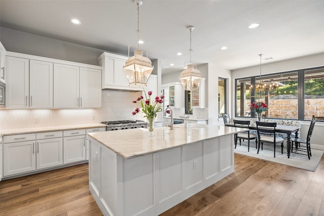 kitchen with white cabinets, decorative light fixtures, decorative backsplash, a kitchen island with sink, and hardwood / wood-style flooring