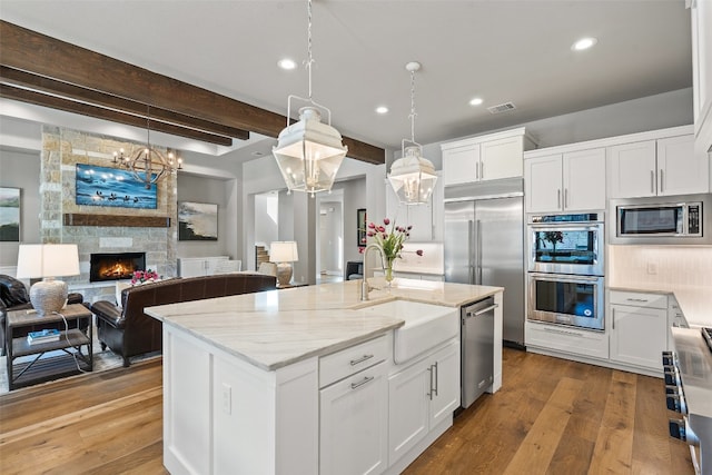 kitchen featuring a fireplace, built in appliances, beamed ceiling, light hardwood / wood-style floors, and a kitchen island with sink