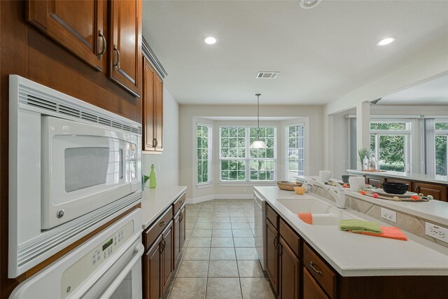 kitchen featuring white appliances, sink, decorative light fixtures, light tile patterned floors, and a center island