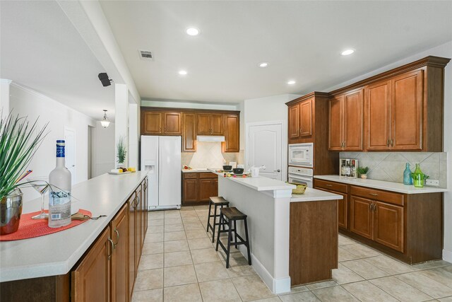 kitchen with tasteful backsplash, white appliances, a center island, a breakfast bar area, and light tile patterned floors