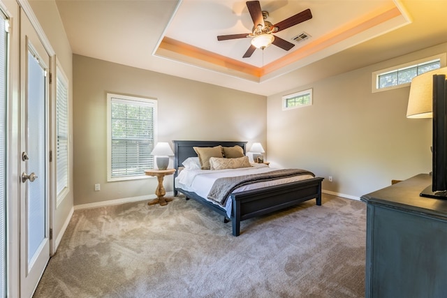 carpeted bedroom with a raised ceiling, ceiling fan, and multiple windows