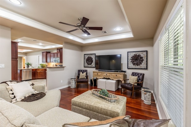 living room featuring dark hardwood / wood-style flooring, ceiling fan, and a raised ceiling