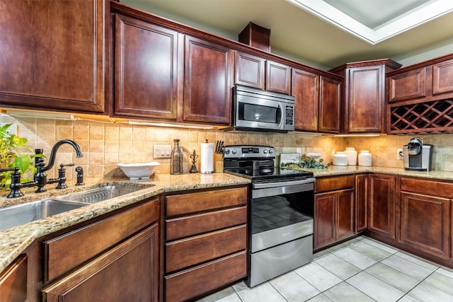 kitchen with light tile patterned floors, stainless steel appliances, light stone counters, sink, and decorative backsplash