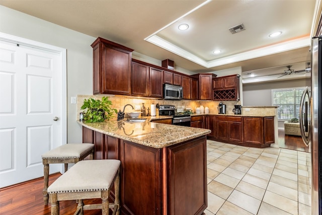 kitchen featuring light hardwood / wood-style flooring, light stone counters, stainless steel appliances, and kitchen peninsula