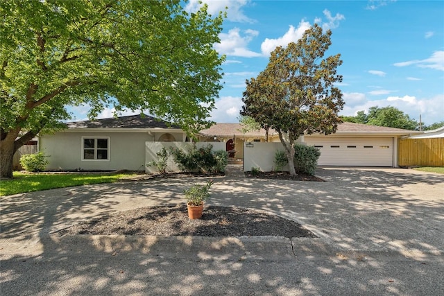 ranch-style house featuring a garage, stucco siding, driveway, and fence