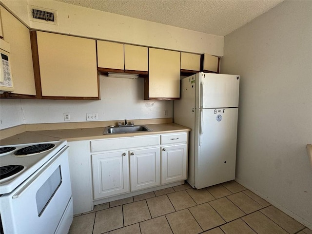 kitchen featuring a textured ceiling, sink, light tile patterned floors, and white appliances