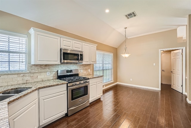 kitchen with decorative backsplash, appliances with stainless steel finishes, vaulted ceiling, pendant lighting, and white cabinetry