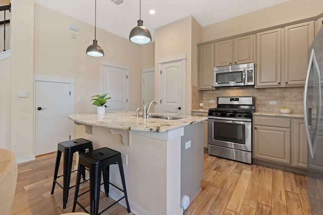 kitchen with sink, hanging light fixtures, light stone countertops, an island with sink, and appliances with stainless steel finishes