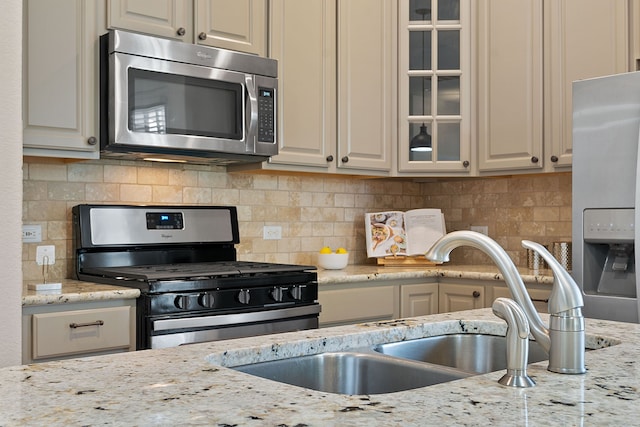 kitchen featuring decorative backsplash, light stone countertops, sink, and stainless steel appliances