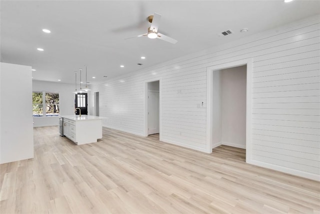 unfurnished living room with ceiling fan, brick wall, and light hardwood / wood-style flooring